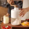 A compact manual ice crusher machine with a hand crank handle on top, filled with finely shaved snow ice.