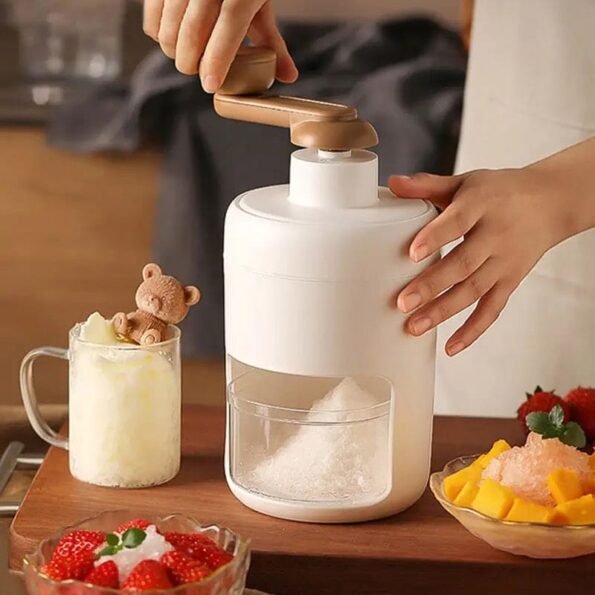 A compact manual ice crusher machine with a hand crank handle on top, filled with finely shaved snow ice.