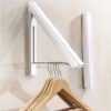 Black metal wall mounted foldable hidden clothes hanger holding laundry in a compact room